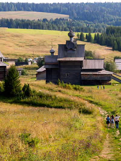 Perm, Russia. A traditional, dark wooden church with tiered roofs and small onion cupolas, situated in a rural landscape.